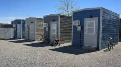 ブロックビルに並ぶ支援付きの小型住宅。灰色の外壁と各戸の玄関が見える