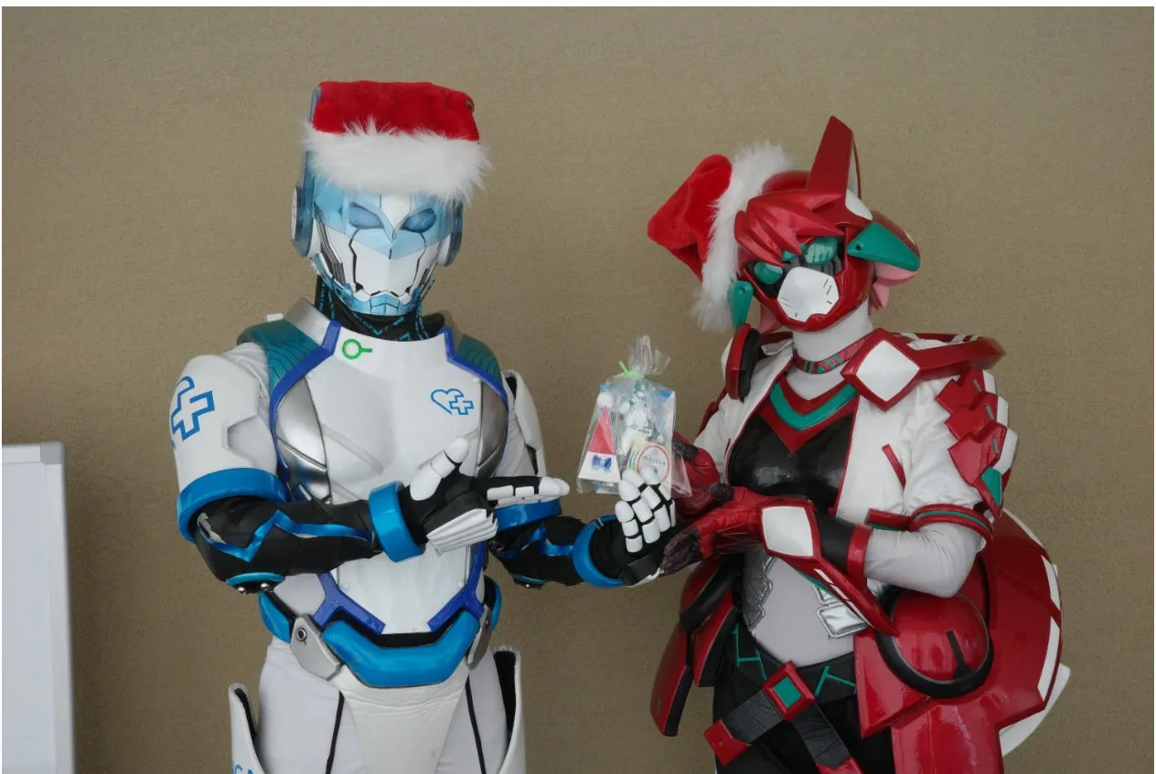 クリスマスの衣装を着たヒーロー2人が、入院中の子どもたちへ贈るプレゼントを手にしている